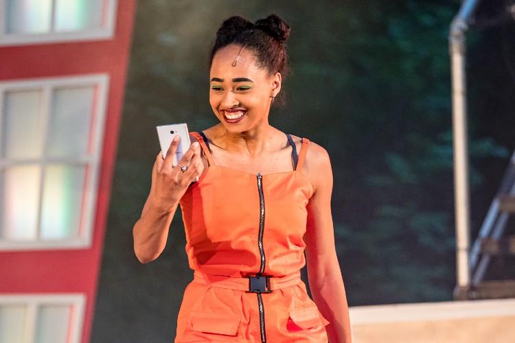 Actor on outdoor stage in orange clothing looking at phone