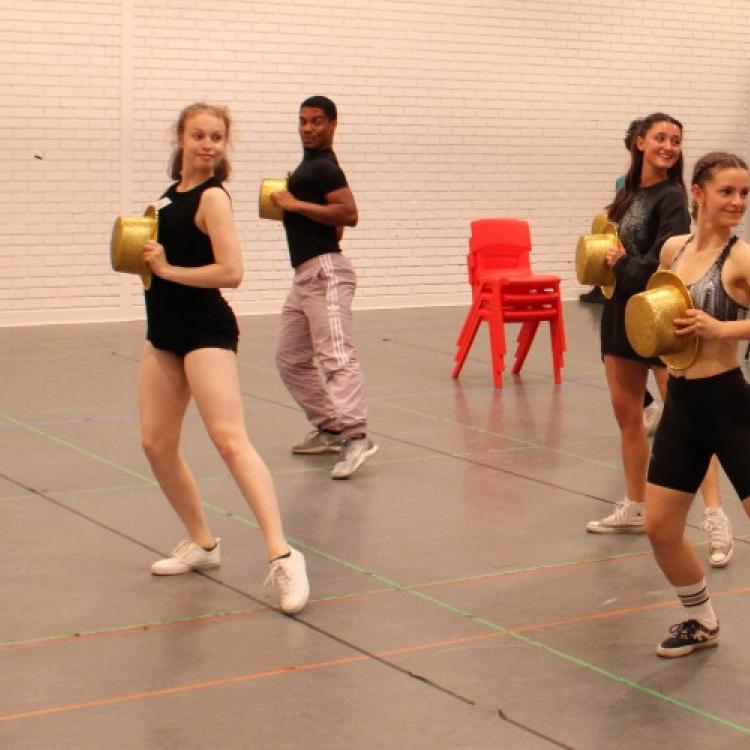 Students holding golden top hats rehearsing a musical